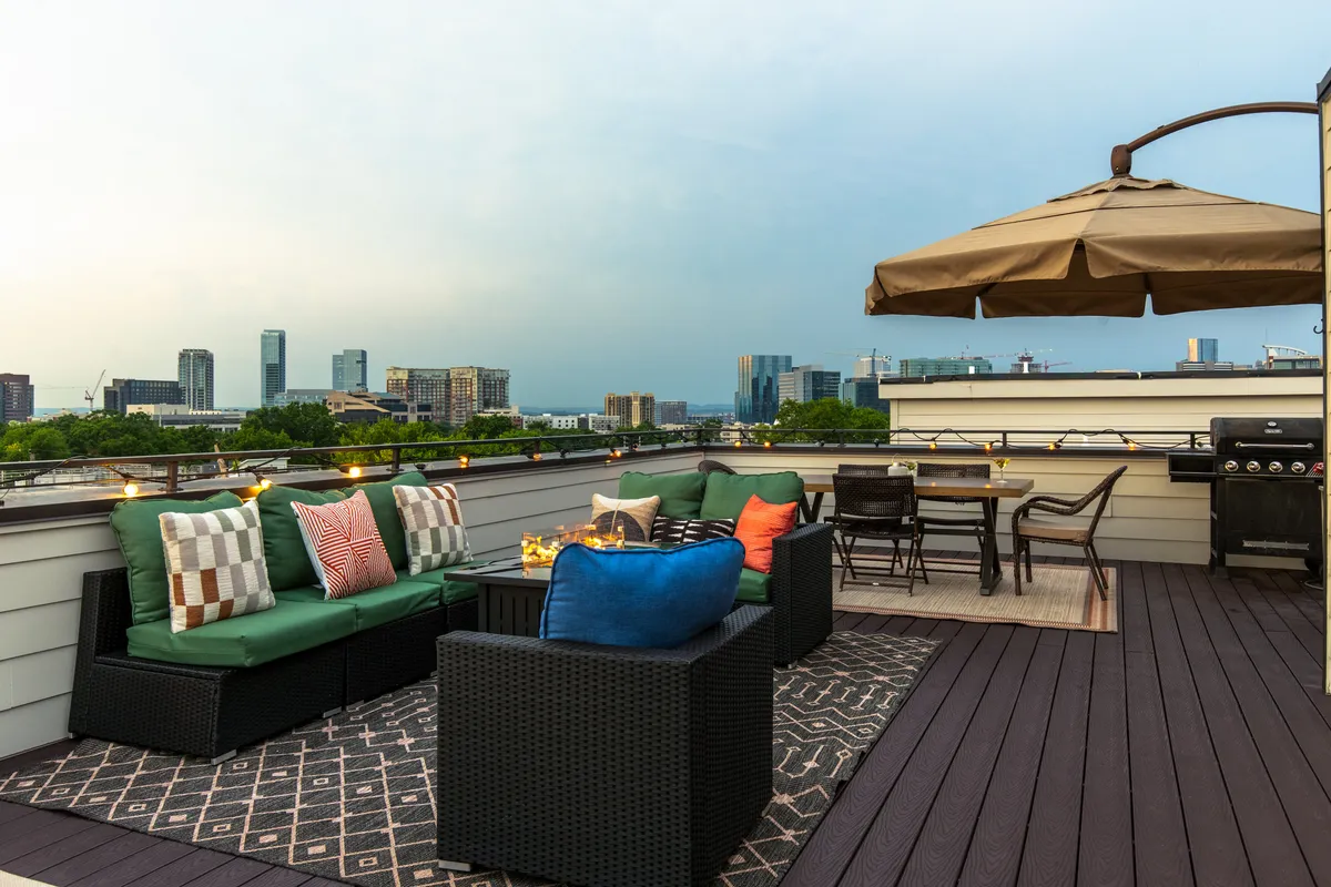 This image showcases a spacious rooftop deck with an outdoor seating area, grill, dining table, and a breathtaking view of the city skyline. The setting is perfect for group gatherings, barbecues, or relaxing evenings, with the city lights creating a stunning backdrop.