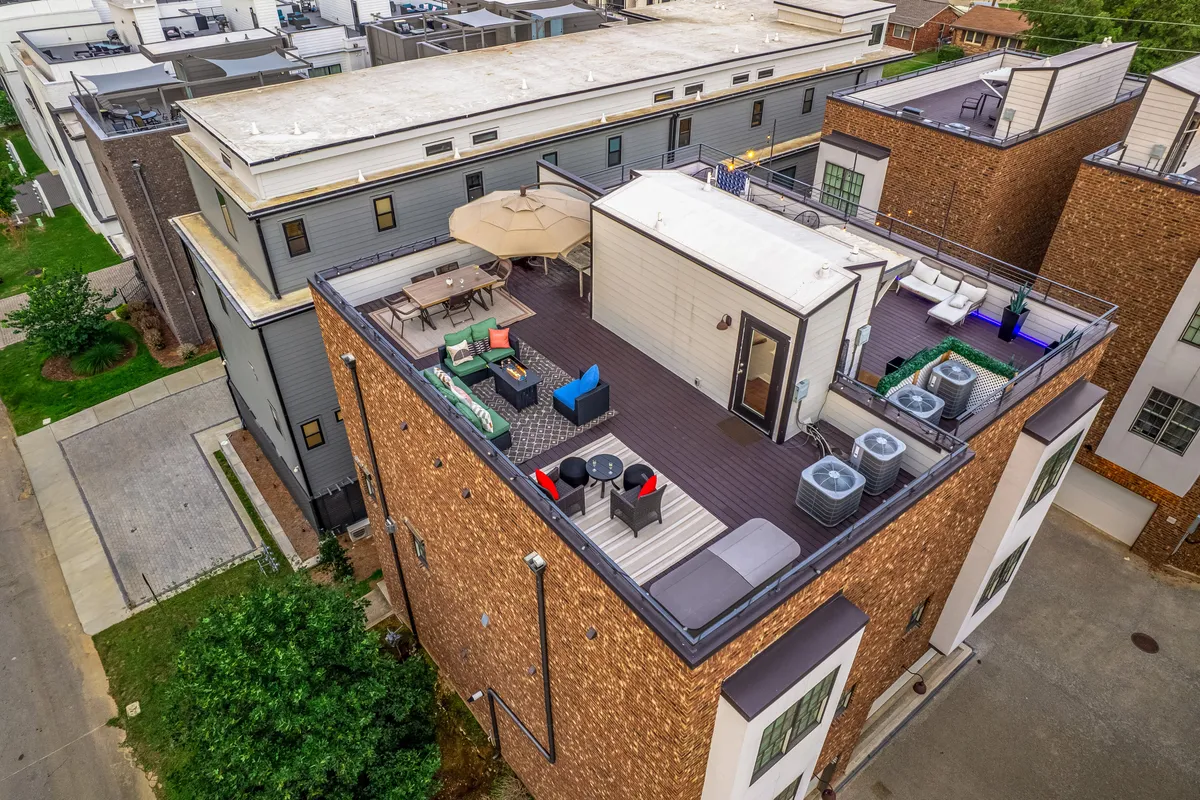 A vibrant rooftop deck featuring outdoor seating, umbrellas for shade, and a communal table, with glimpses of the city skyline in the distance. The space is designed for both relaxation and entertaining, offering plenty of room for socializing or enjoying a meal outdoors as the sun sets.