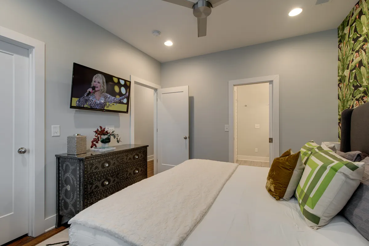 A comfortable bedroom scene featuring a bed with decorative pillows, a wall-mounted television, and a decorative dresser. The soft lighting and plush bedding create a cozy, restful atmosphere perfect for unwinding.