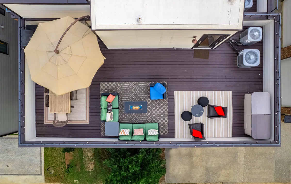 A spacious outdoor area with a dining table, parasol, comfortable seating, and a fire pit, all set against a backdrop ideal for al fresco dining and evening gatherings. The scene is casual and comfortable, inviting guests to imagine socializing or relaxing in a well-maintained setting.