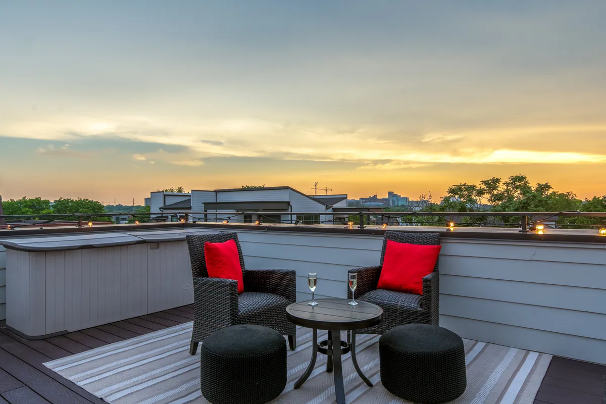 An inviting outdoor seating area featuring two chairs with red cushions and a small round table set with two champagne glasses. The setup is placed to capture a beautiful sunset, suggesting a private and peaceful atmosphere.