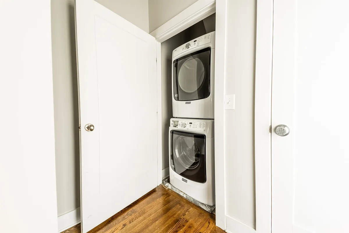 A practical laundry area with stacked washer and dryer, white doors, and wooden flooring. The space is clean and efficiently designed, ready for everyday tasks and contributing to seamless living.